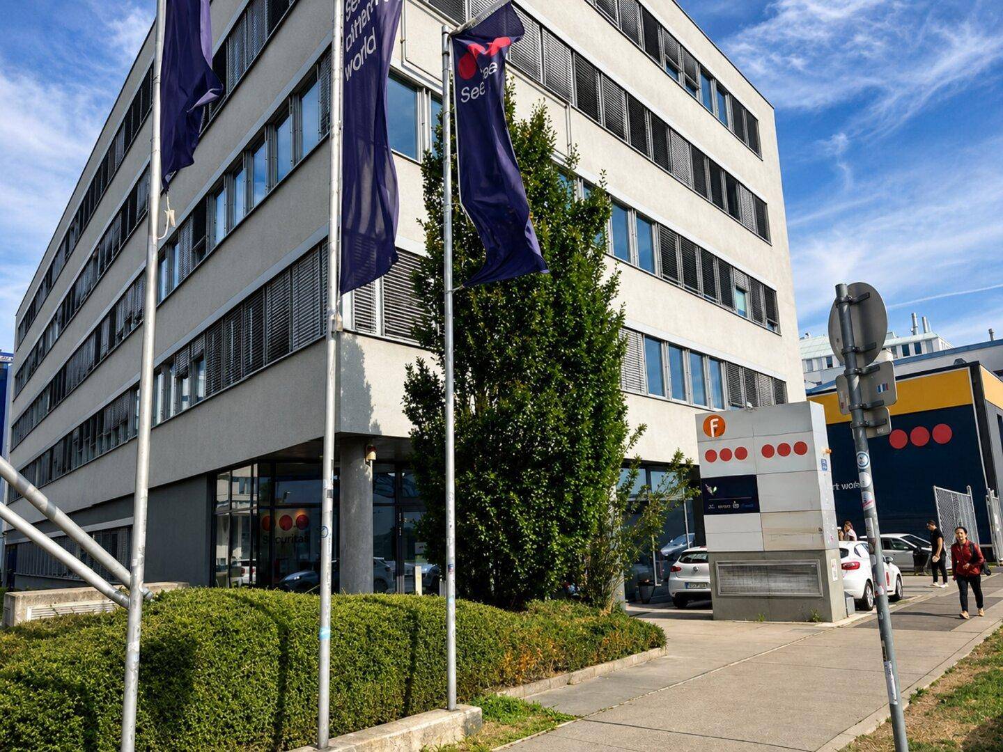 Die moderne Fassade des Bürogebäudes ist von gepflegten Grünflächen und Fahnenmasten umgeben.