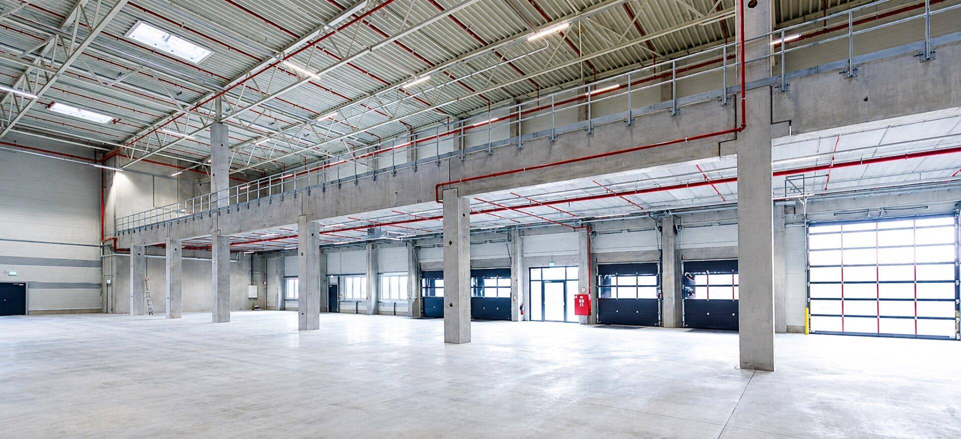 Geräumige Industriehalle mit Betonboden, hohen Decken, Laderampen und einer Zwischenebene für Büros oder Lager.