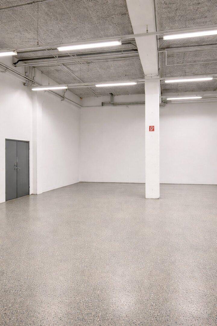 Leerer Industrieraum mit hellem Terrazzoboden, weiß gestrichenen Wänden und hoher Decke.