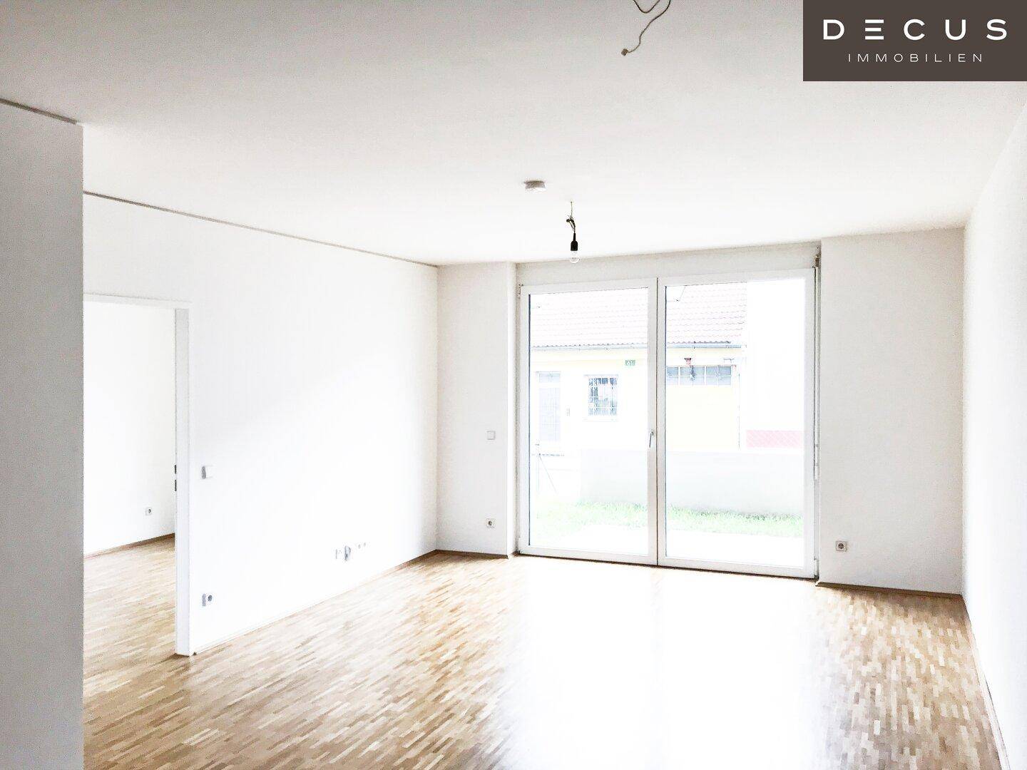 Heller leerer Raum mit Parkettboden und großen Schiebetüren zum Außenbereich.