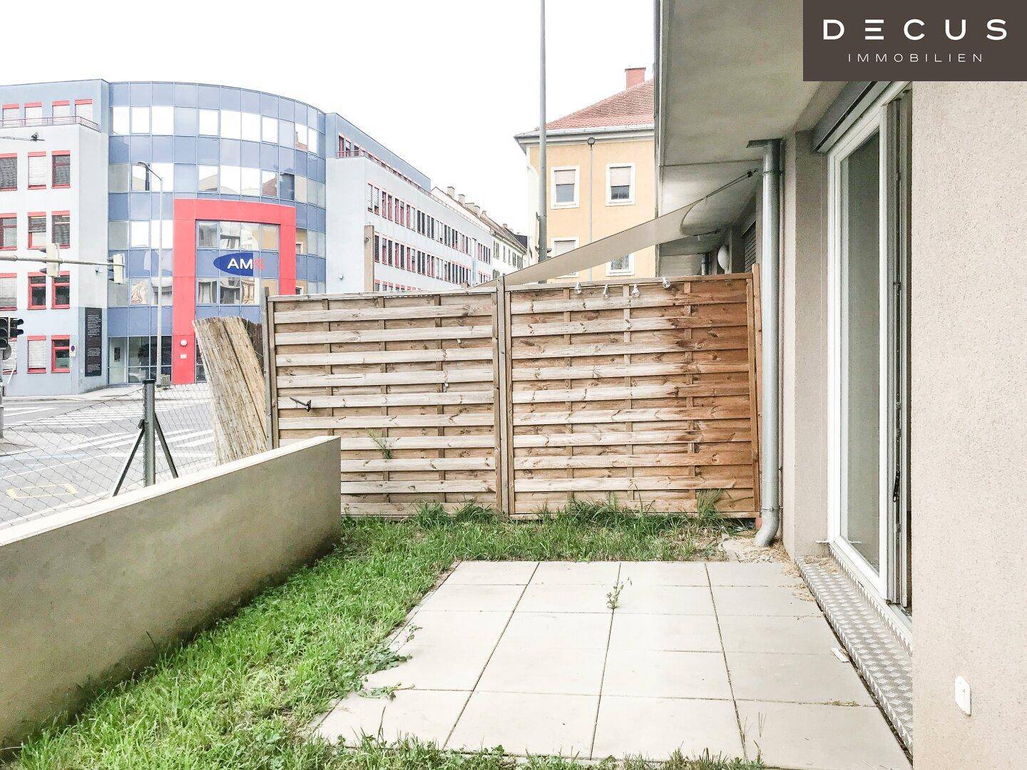 Kleine gepflasterte Terrasse mit Rasenfläche und Holzzaun, angrenzend an das Gebäude.