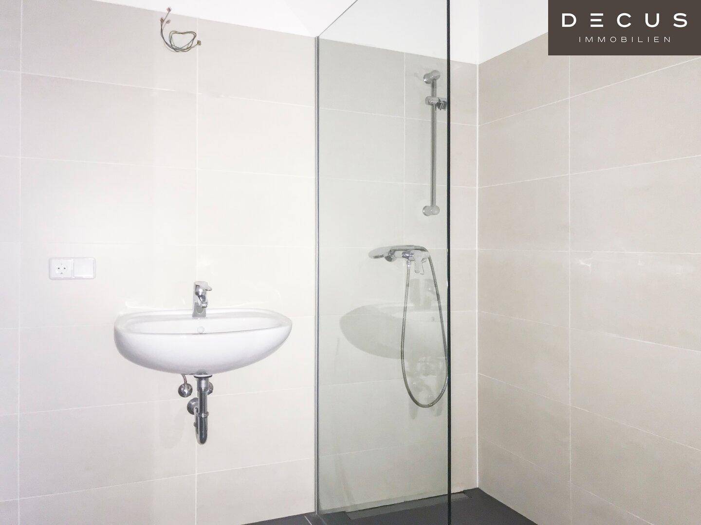Modernes Badezimmer mit Waschbecken, Glasdusche und hellen Wandfliesen.