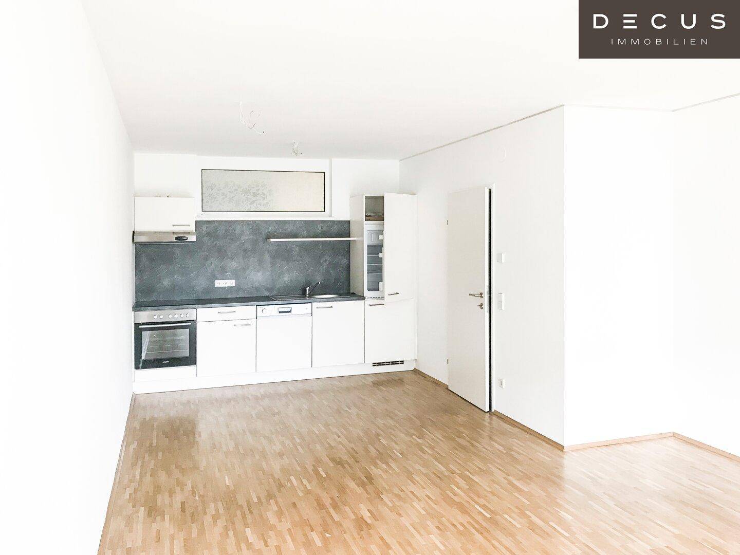 Offener Küchenbereich mit weißen Schränken, dunkler Arbeitsplatte und Holzfußboden.