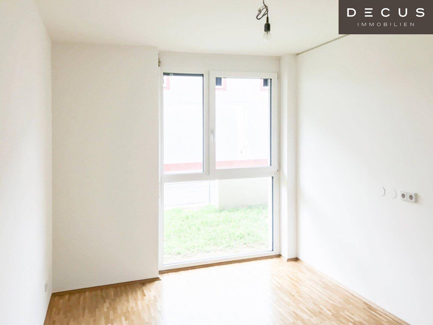 Heller Raum mit Parkettboden und großem Fenster mit Blick auf den Außenbereich.