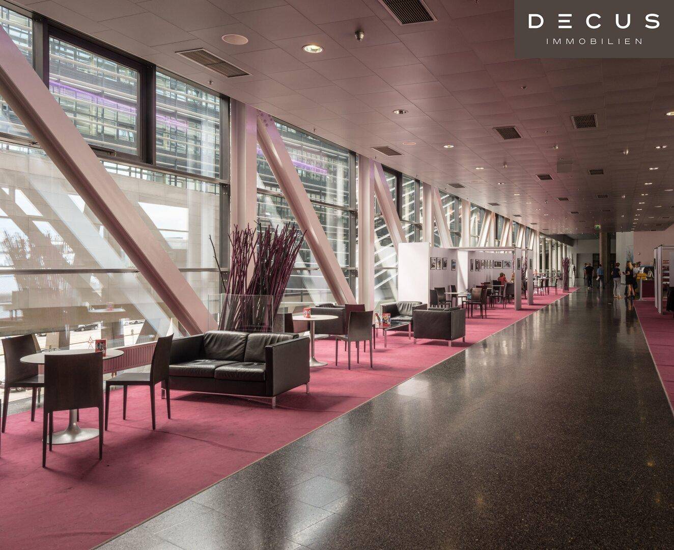 Moderner Loungebereich mit bequemen Sofas, Tischen und großen Fenstern mit Blick nach draußen.