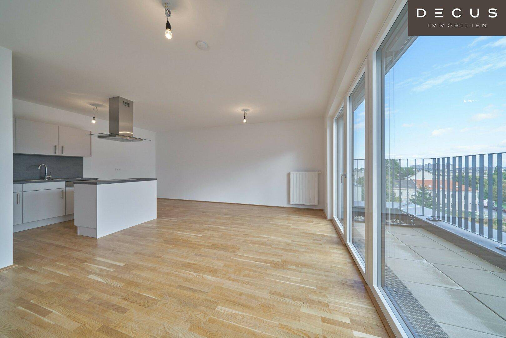 Heller offener Wohnbereich mit integrierter Küche, Parkettboden und Zugang zu einem großen Balkon.