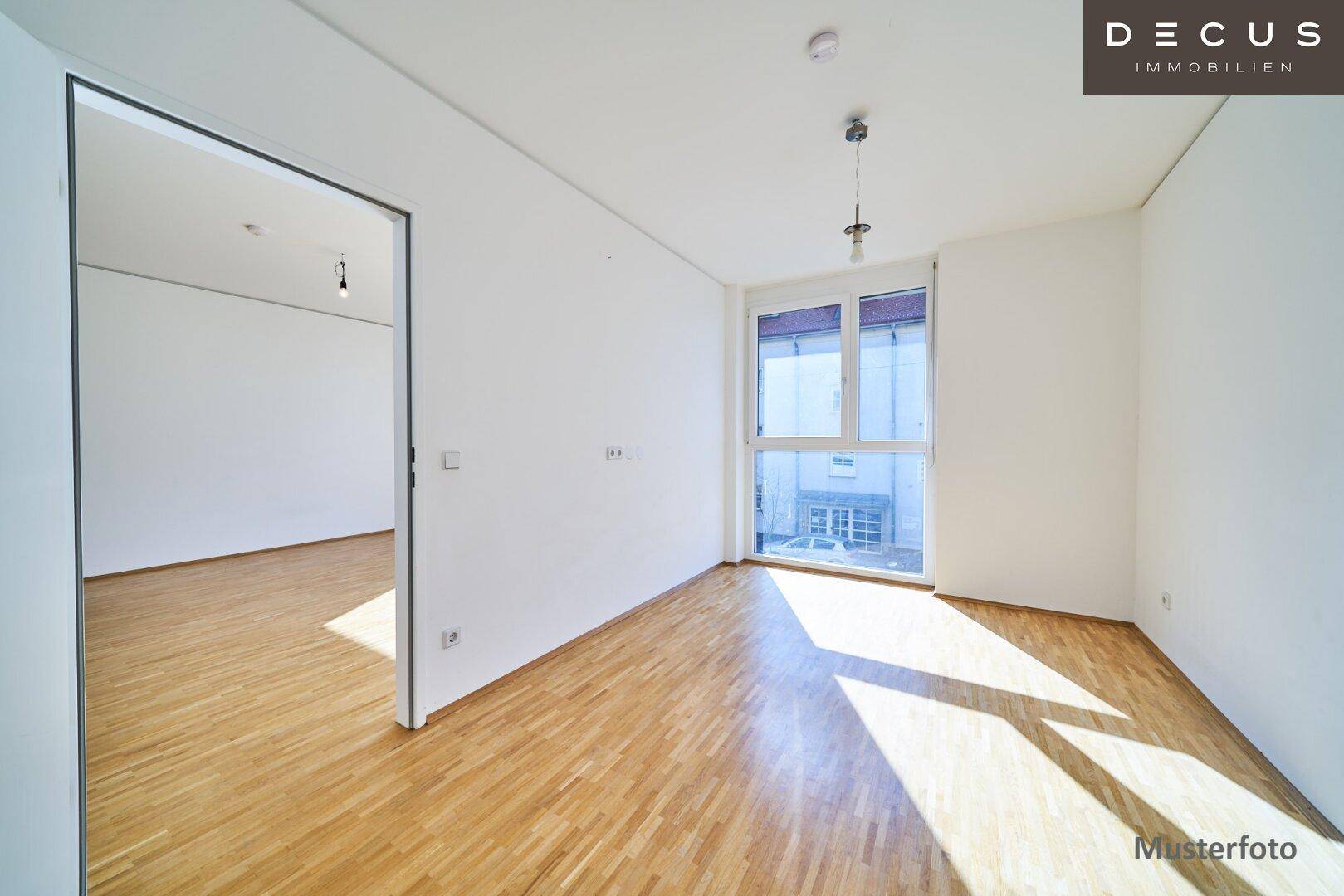 Helles Zimmer mit Parkettboden und großen Fenstern, das viel Tageslicht hereinlässt.
