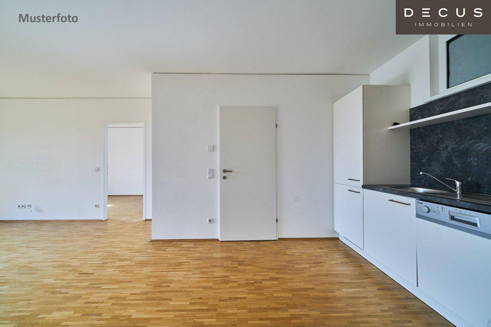 Wohnbereich mit integrierter Küchenzeile und Zugang zu einem weiteren Zimmer, mit Parkettboden.