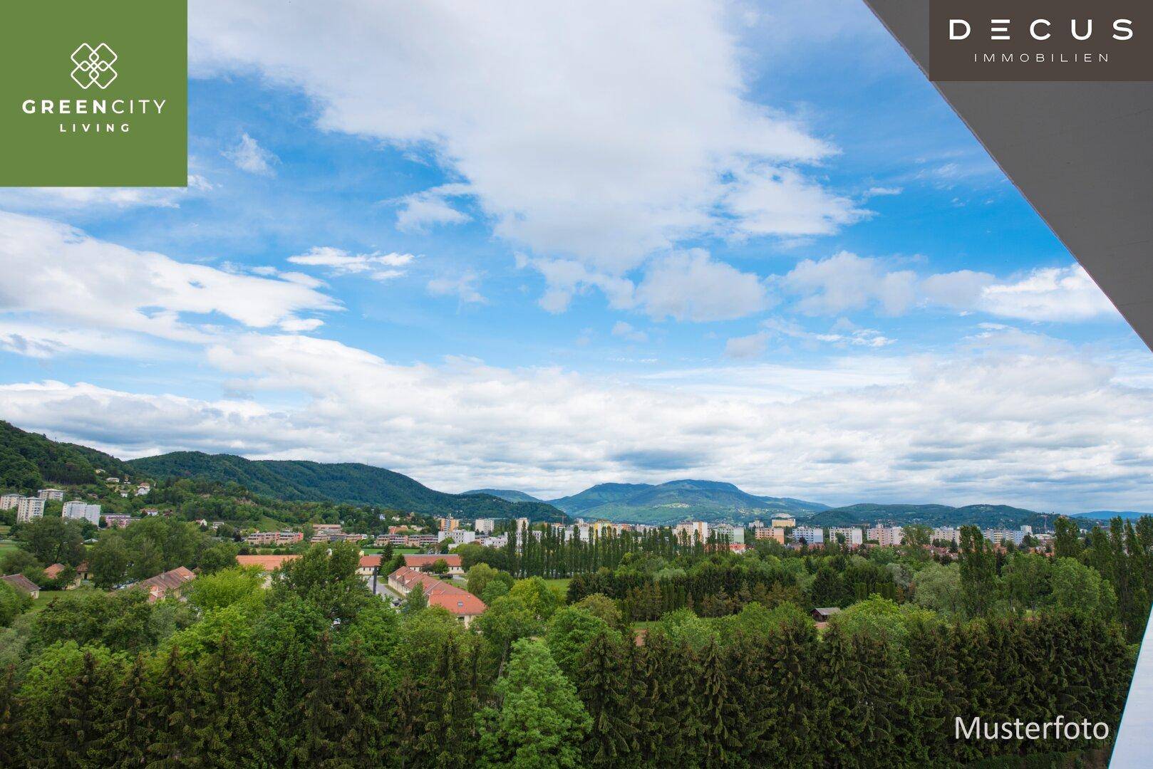 Weitläufiger Blick über eine grüne Landschaft mit Bergen und städtischer Bebauung.
