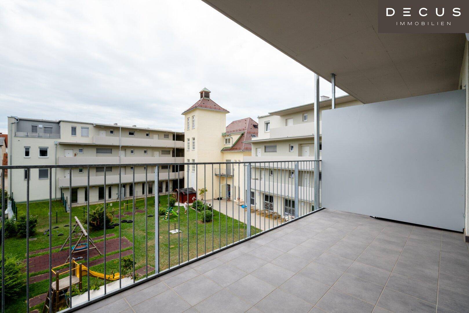 Gefliester Balkon mit Blick auf den gemeinschaftlichen Innenhof und den Kinderspielplatz.