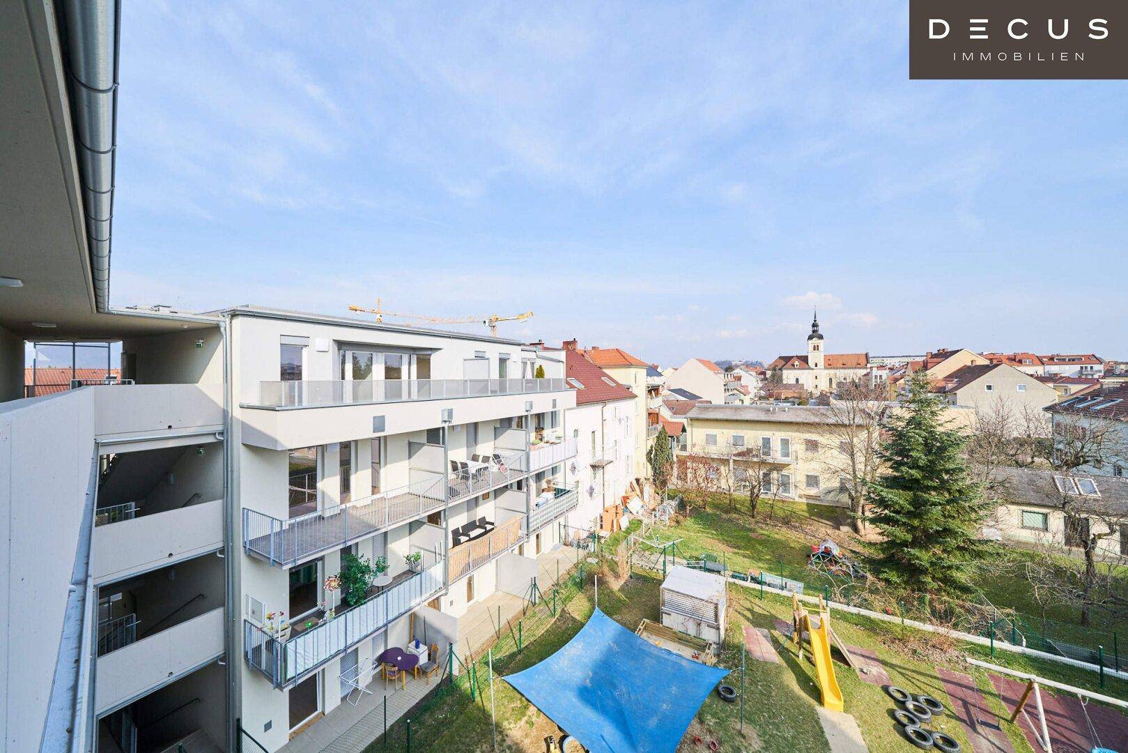 Panoramablick auf die moderne Wohnanlage mit Balkonen, Spielplatz und der umliegenden Stadtlandschaft.