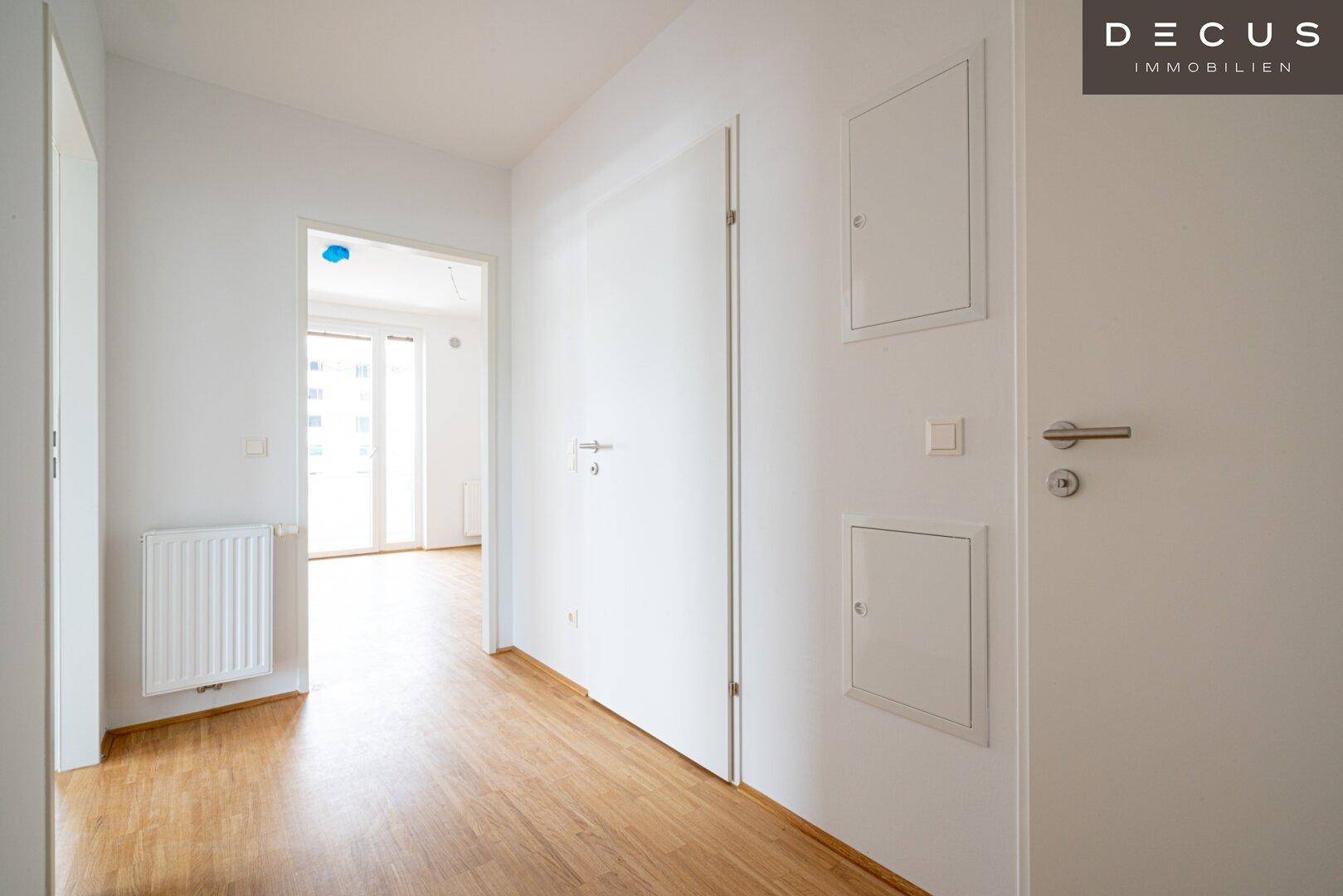 Heller Flur mit Holzboden und weißen Wänden, der zu weiteren Räumen führt.
