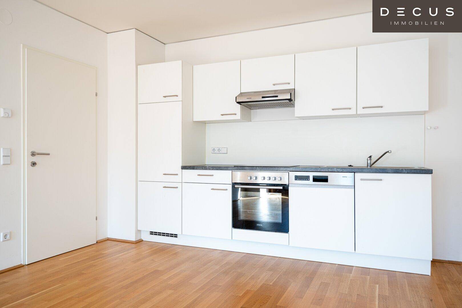 Moderne Einbauküche mit weißen Schränken, integrierten Geräten und dunkler Arbeitsplatte.