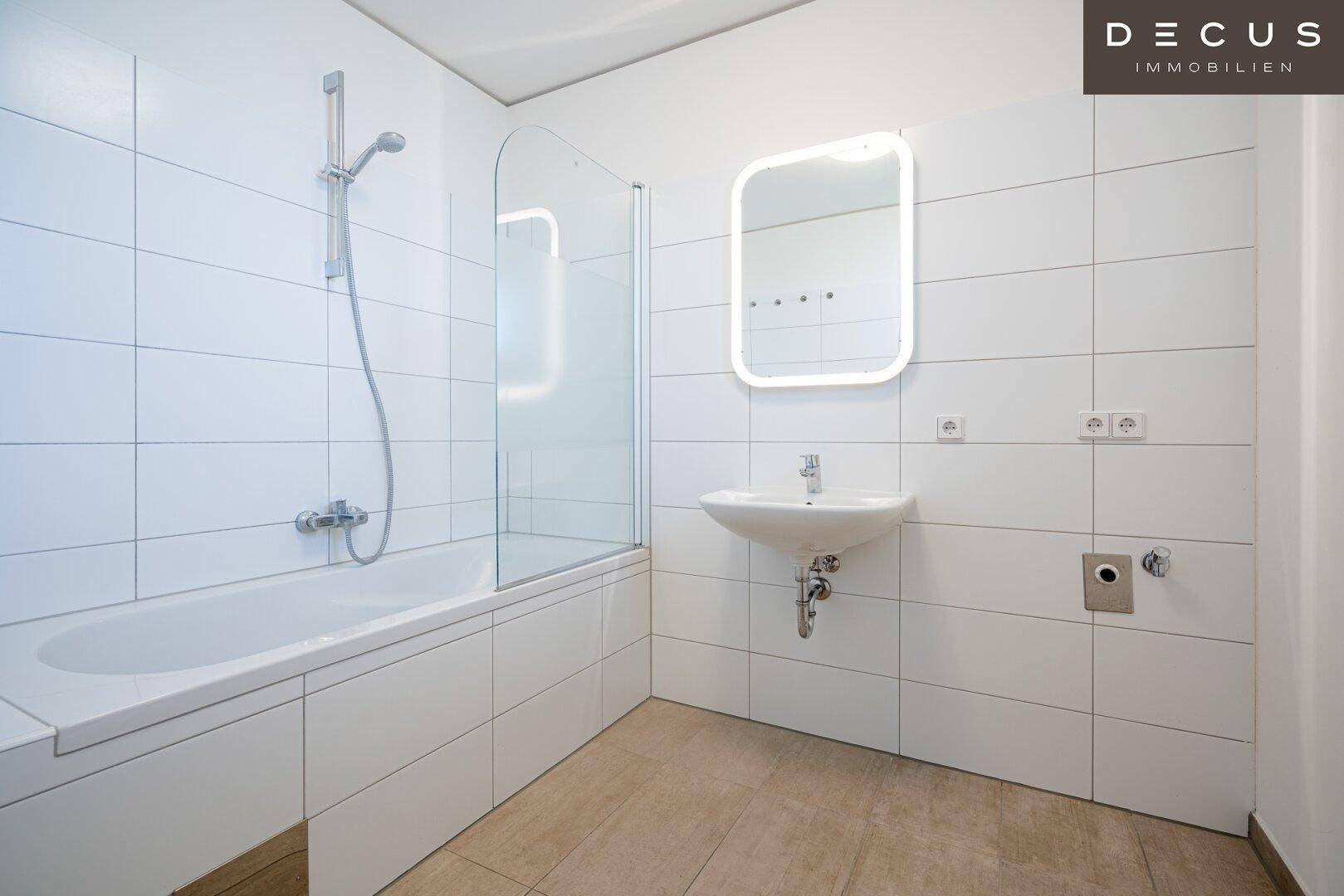 Modernes Badezimmer mit Badewanne, Duschabtrennung, Waschbecken und großformatigen weißen Fliesen.