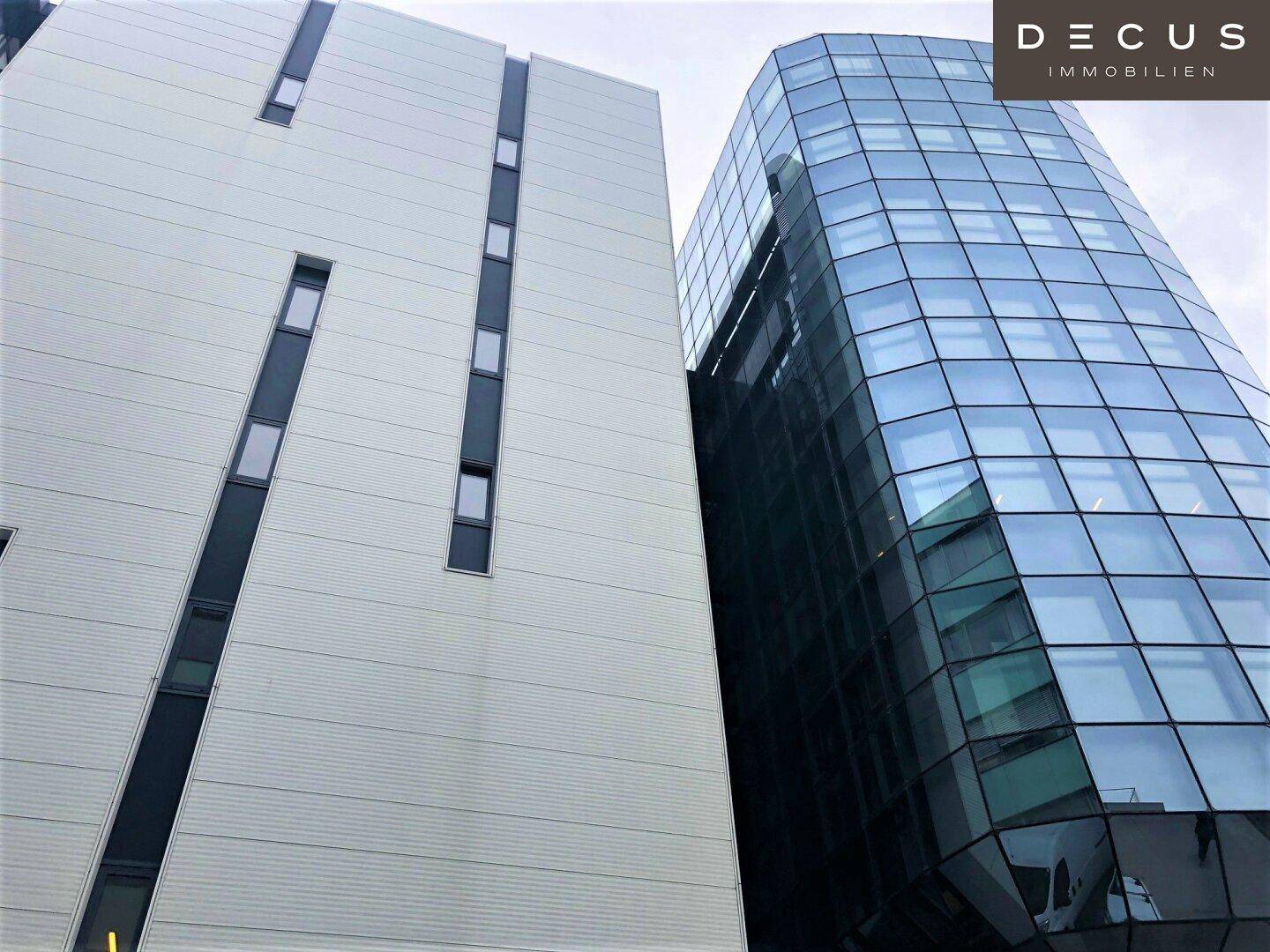 Ansicht eines modernen Bürokomplexes mit einer markanten Glasfassade und einer hellen, strukturierten Außenwand.