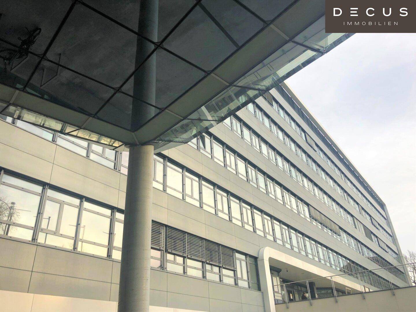 Fassade eines Bürogebäudes mit zahlreichen Fenstern und einem modernen Glasvordach, das den Eingangsbereich schützt.