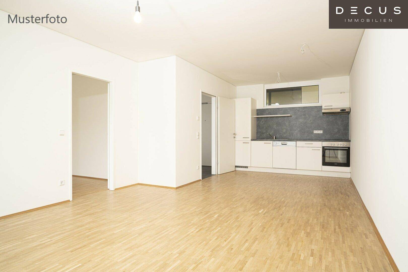 Offener Wohnbereich mit integrierter, einfacher Küchenzeile und hellem Parkettboden.