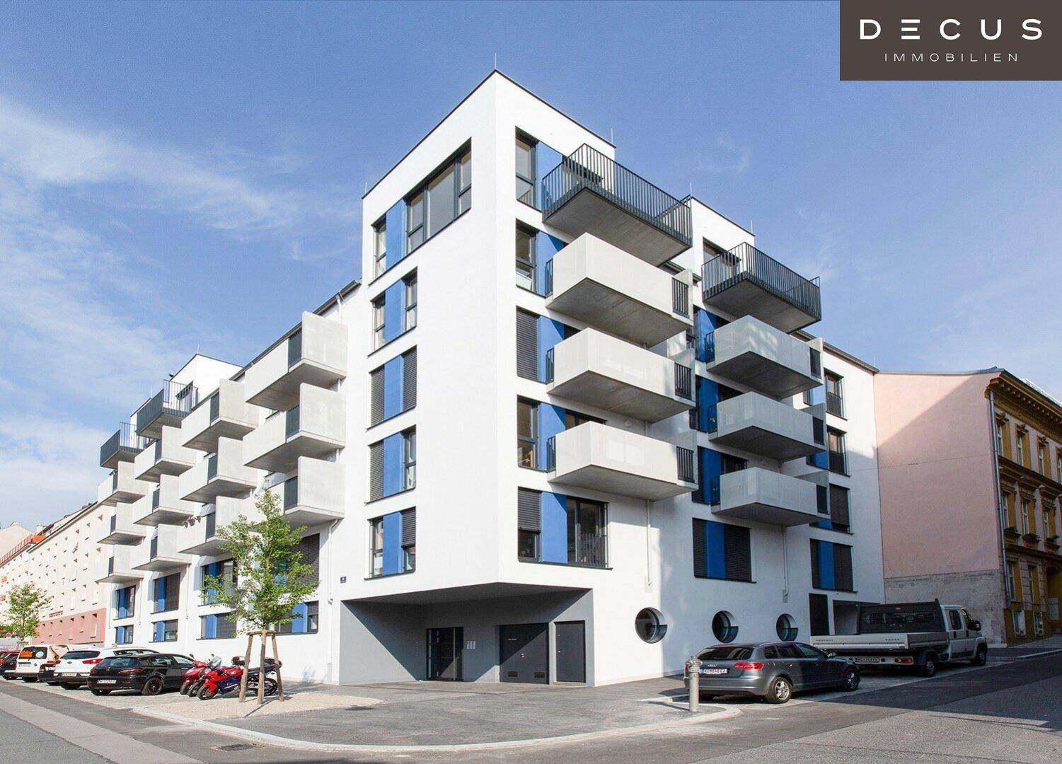 Modernes Mehrfamilienhaus mit weißer Fassade, blauen Akzenten und zahlreichen Balkonen in urbaner Umgebung.