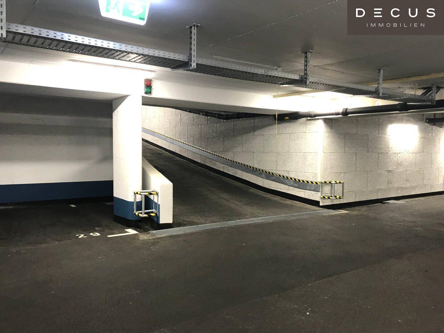 Zufahrtsrampe zur Tiefgarage mit Sicherheitsmarkierungen und heller Beleuchtung, bereit für Fahrzeuge.