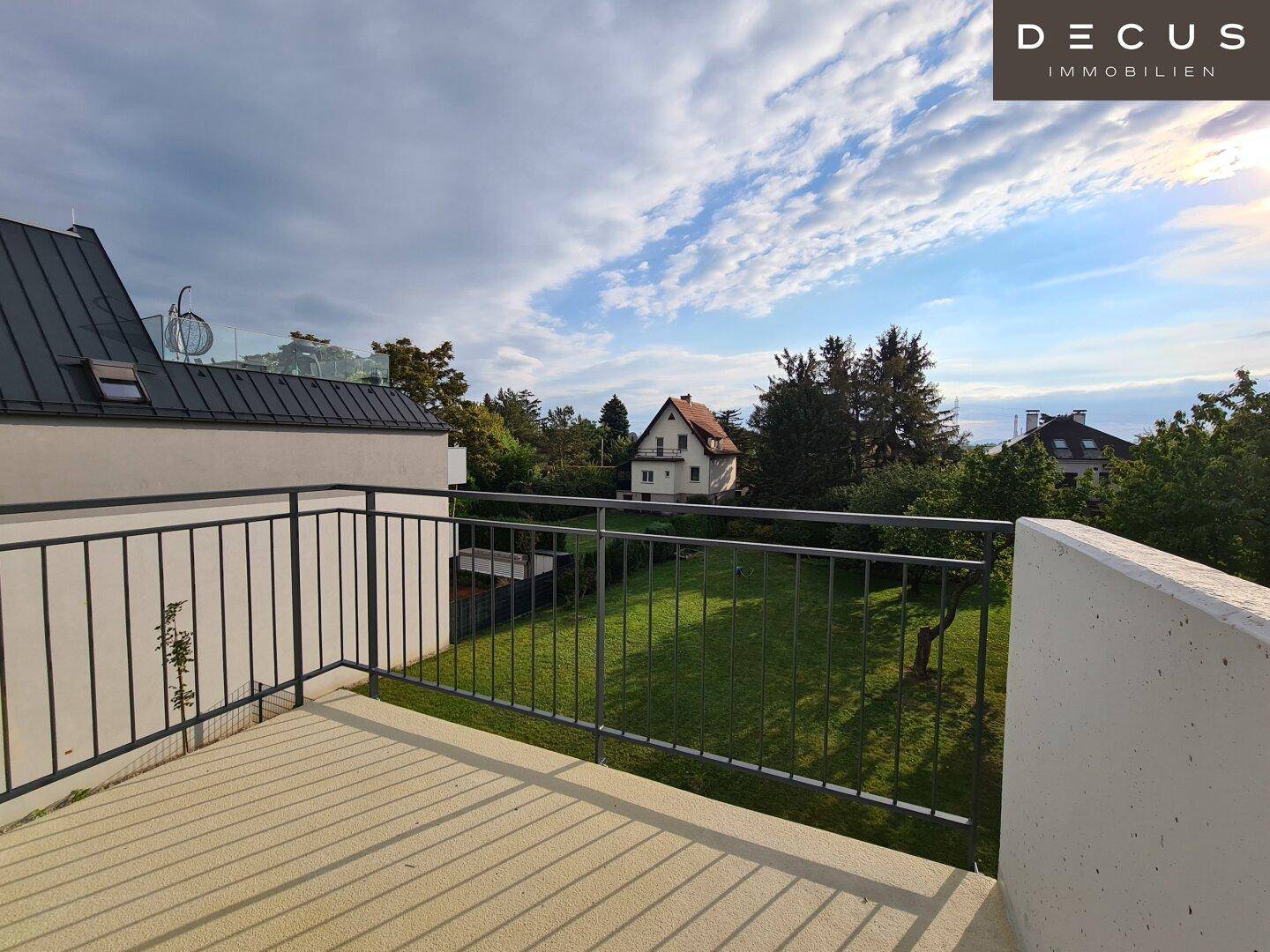 Geräumige Terrasse mit Metallgeländer und weitem Blick über grüne Gärten und Häuser.