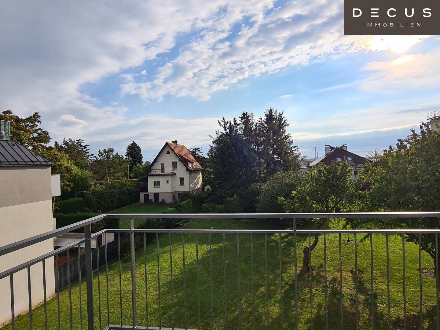 Blick von einem Balkon auf eine grüne Wiese und weitere Häuser in der Ferne.