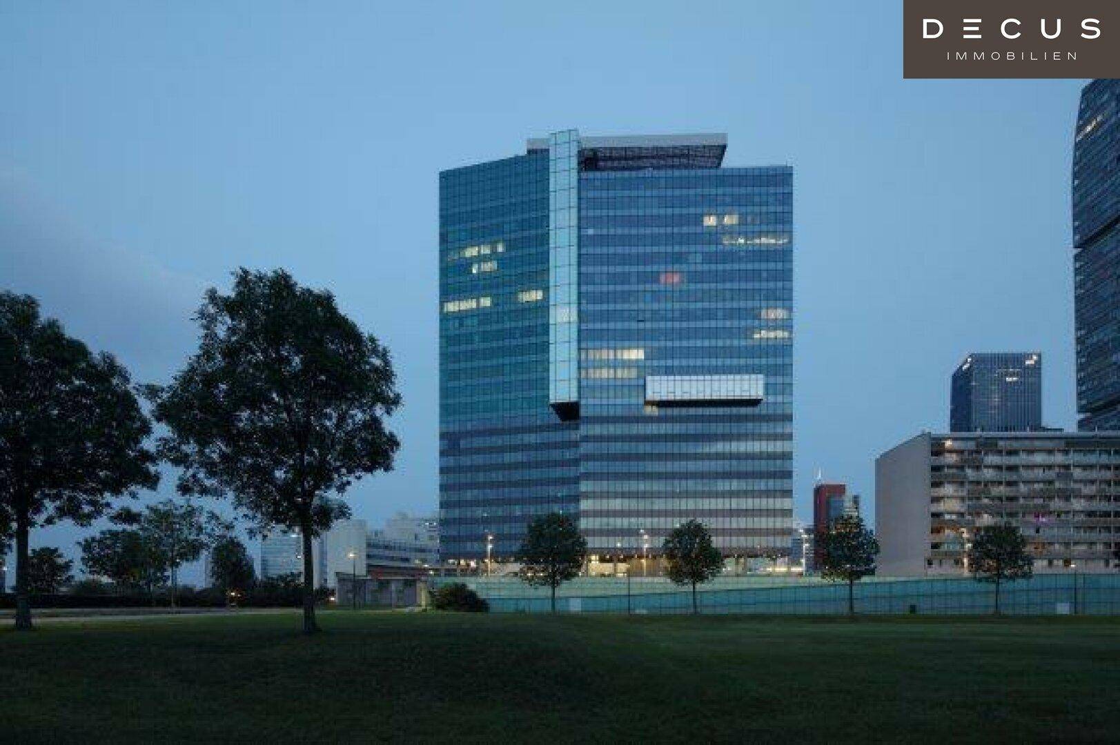 Modernes Hochhaus mit Glasfassade und umliegenden Grünflächen in der Abenddämmerung.