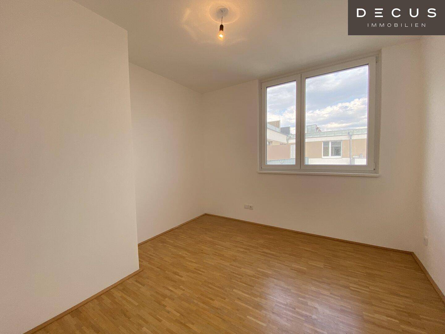 Geräumiges Schlafzimmer mit Holzparkett und großem Fenster für viel Tageslicht.