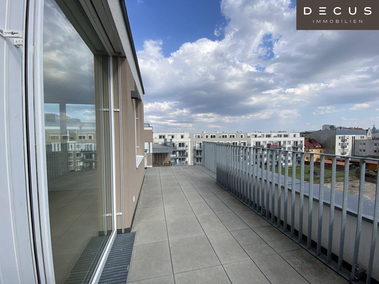 Weitläufige Dachterrasse mit Fliesenboden und Blick auf die umliegende Stadtlandschaft.