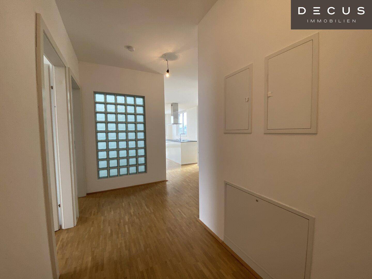 Heller Flur mit Parkettboden und dekorativer Glasbausteinwand, die zur Küche führt.
