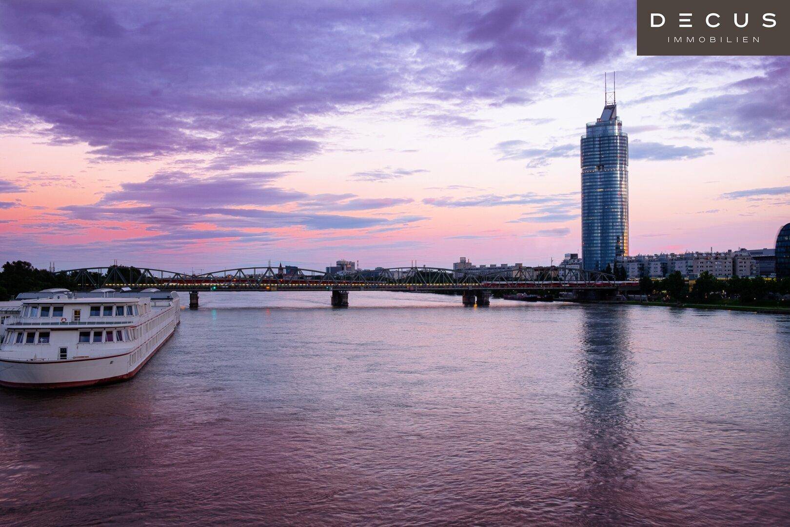 Panoramablick auf eine Stadt bei Sonnenuntergang mit einem Fluss, einer Brücke und einem modernen Wolkenkratzer.