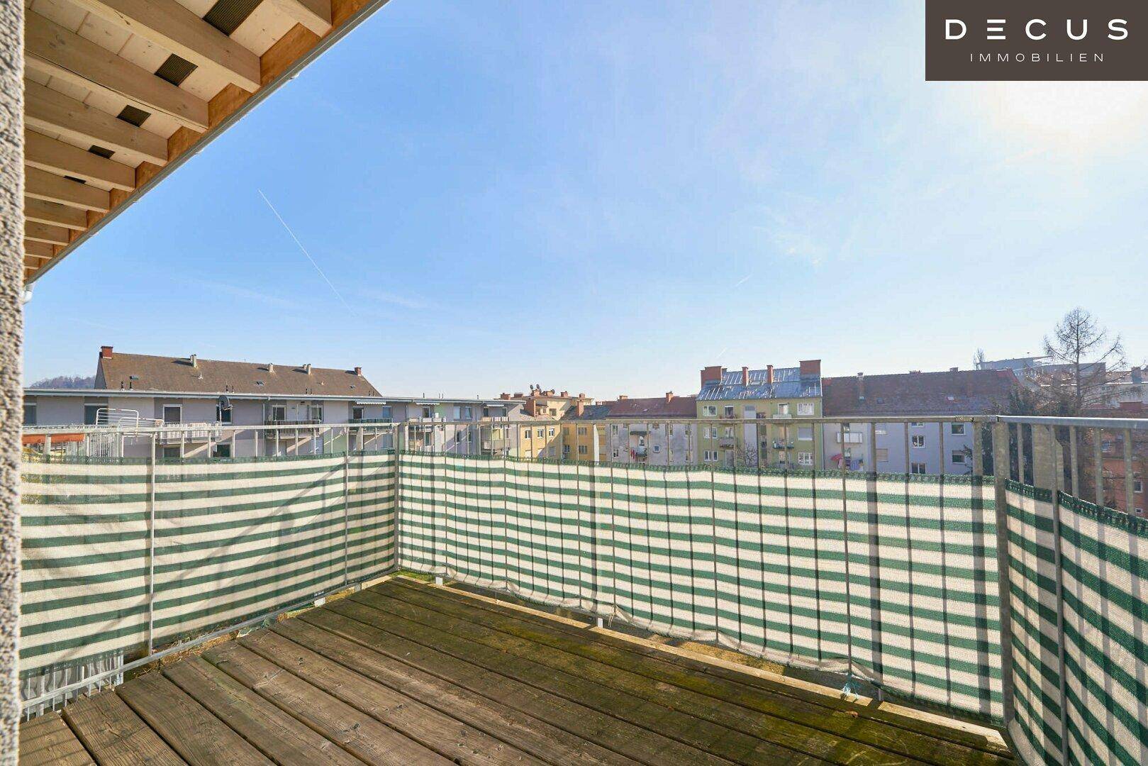 Geräumiger Balkon mit Holzboden und gestreiftem Sichtschutz, bietet Blick auf umliegende Gebäude.
