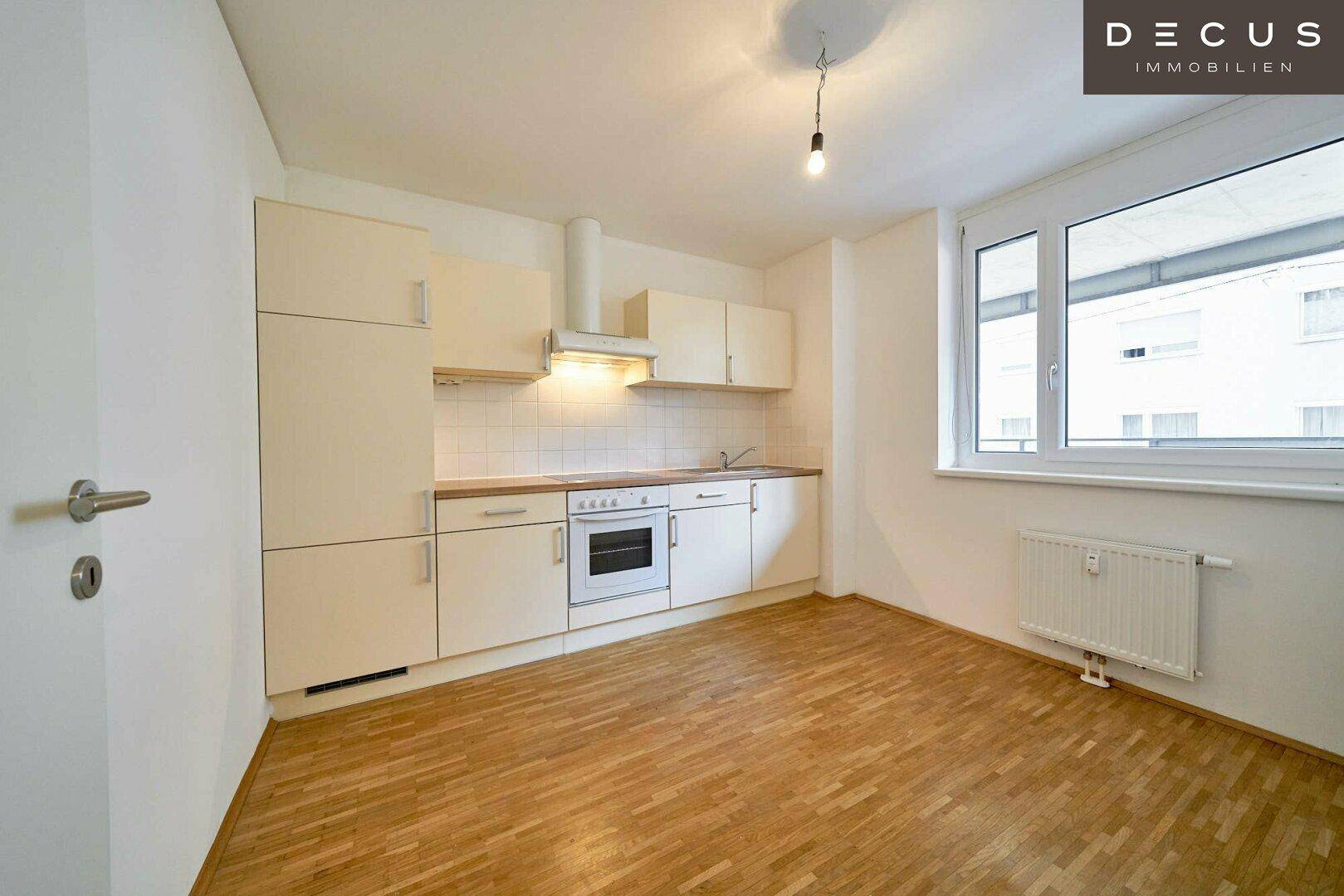 Funktionale Küchenzeile mit hellen Schränken, Holzarbeitsplatte und Fenster, ideal für kleine Räume.