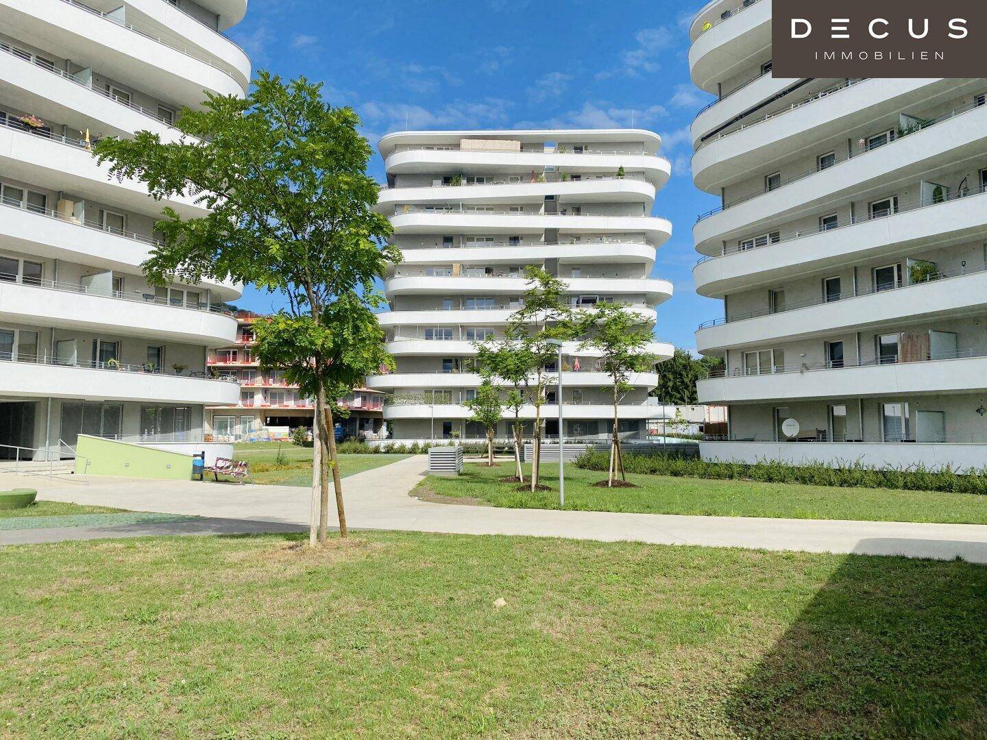 Mehrere moderne Gebäude mit geschwungenen Balkonen und gepflegten Grünflächen im Vordergrund.