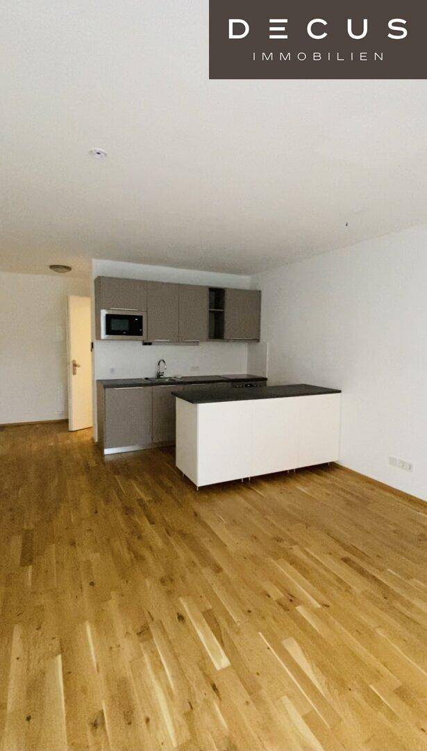 Offene Küchenzeile mit Kücheninsel und hellem Holzparkett in einem modernen Wohnraum.
