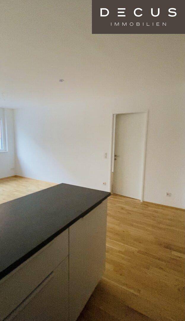 Blick auf eine moderne Kücheninsel mit dunkler Arbeitsplatte und hellem Holzparkett.