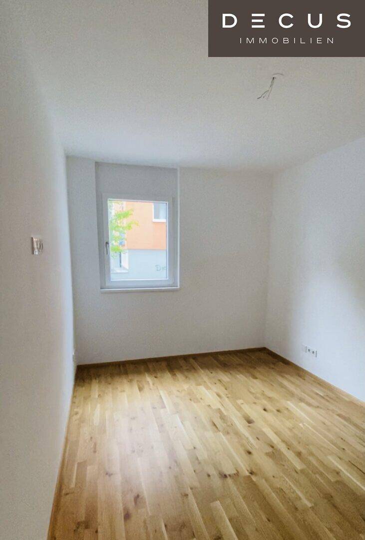 Helles Schlafzimmer mit Fenster und Holzparkett, ideal für eine ruhige Wohnatmosphäre.
