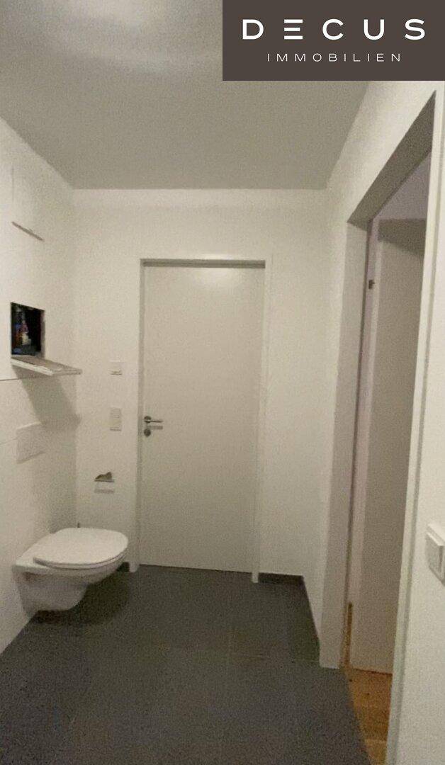 Separate Toilette mit Wand-WC und dunklen Bodenfliesen, schlicht und funktional.