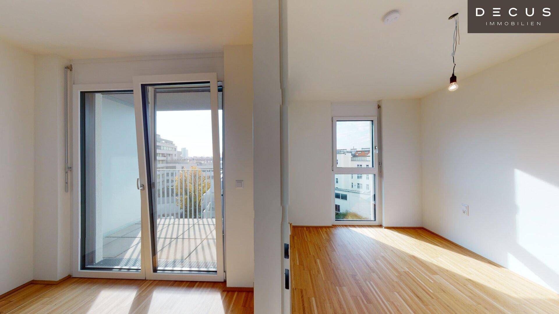 Heller Wohnraum mit großen Schiebetüren zum Balkon und einem weiteren Fenster, ausgestattet mit Parkettboden.