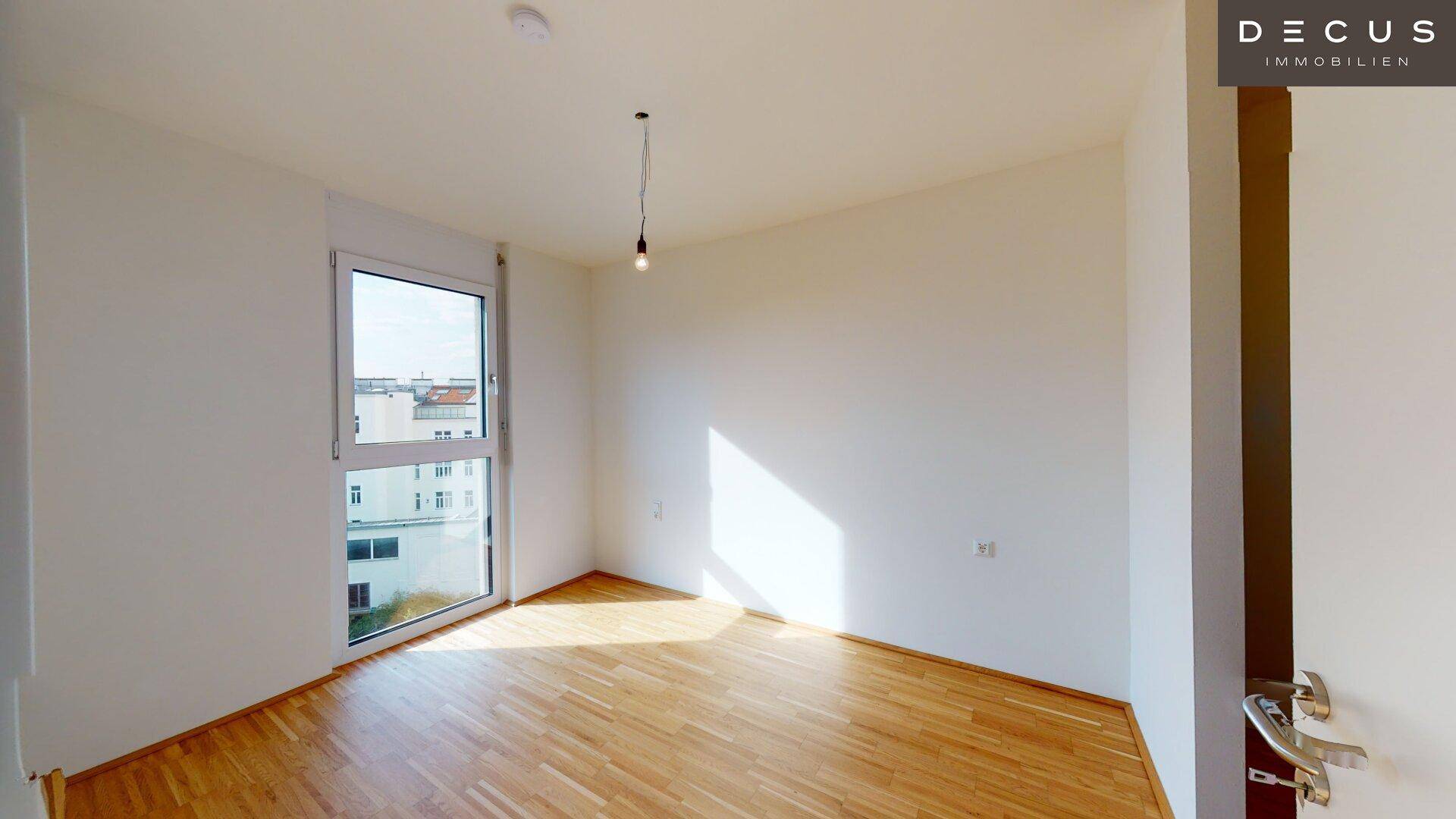 Helles Schlafzimmer mit großem Fenster, das viel Tageslicht hereinlässt, und einem warmen Parkettboden.