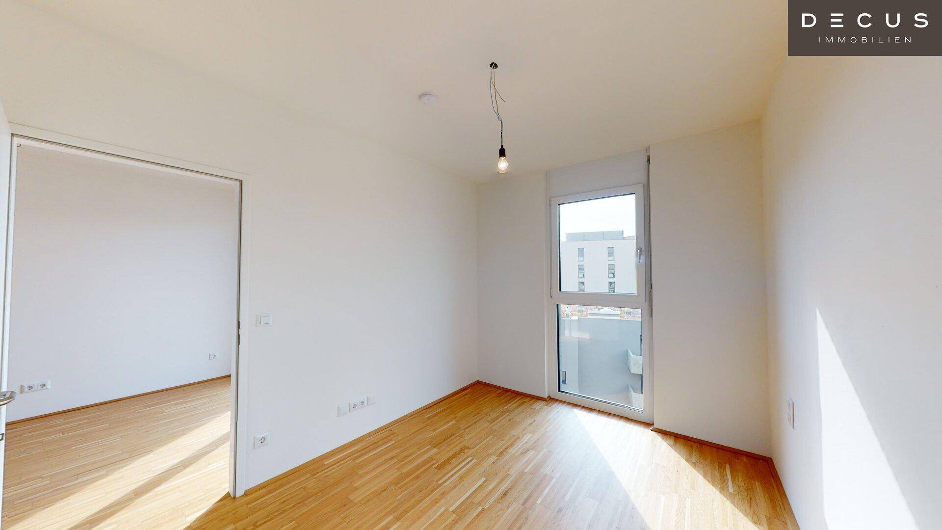 Geräumiges Zimmer mit hellem Parkettboden und einem großen Fenster, das einen Blick nach draußen bietet.