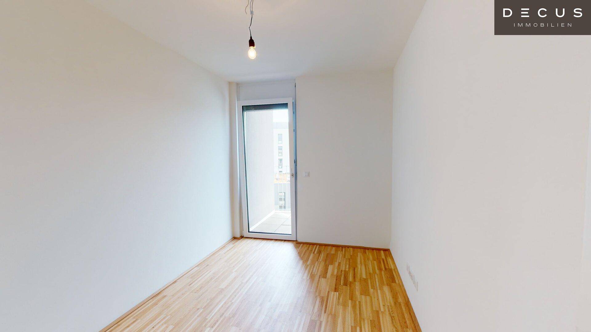 Helles Schlafzimmer mit Parkettboden und Zugang zu einem Balkon, bietet viel Tageslicht.