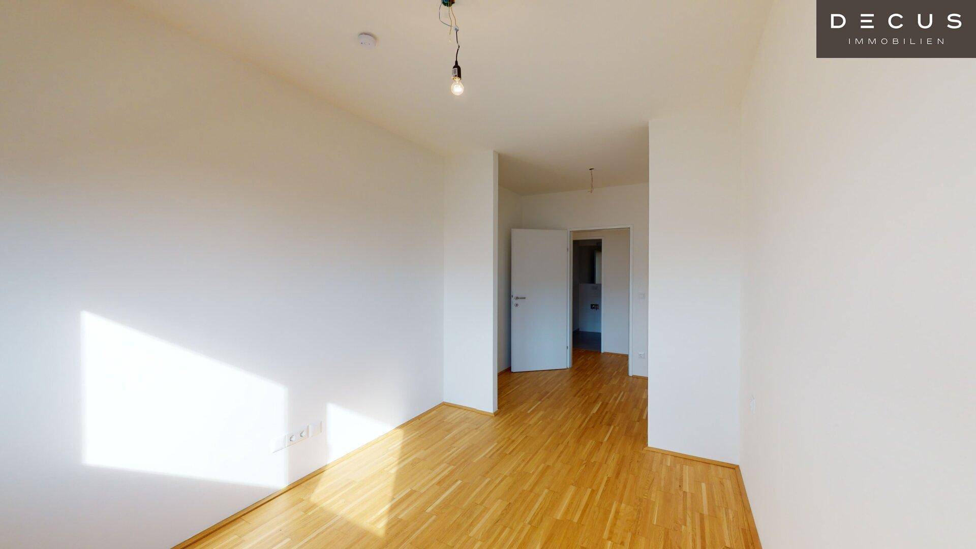 Lichtdurchflutetes Zimmer mit Parkettboden und großen Fenstern, ideal als Schlaf- oder Arbeitszimmer.