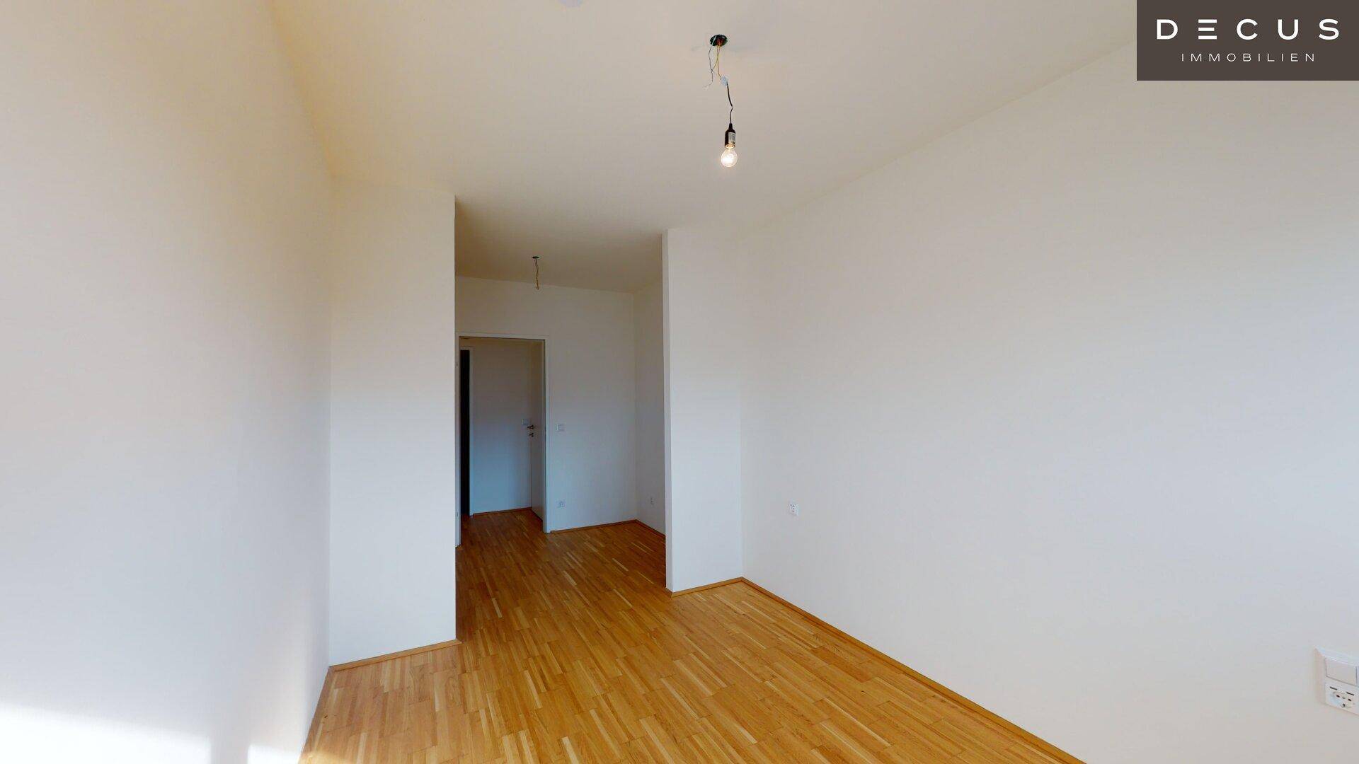 Helles Zimmer mit Parkettboden und Zugang zu einem weiteren Raum, bietet vielseitige Nutzungsmöglichkeiten.