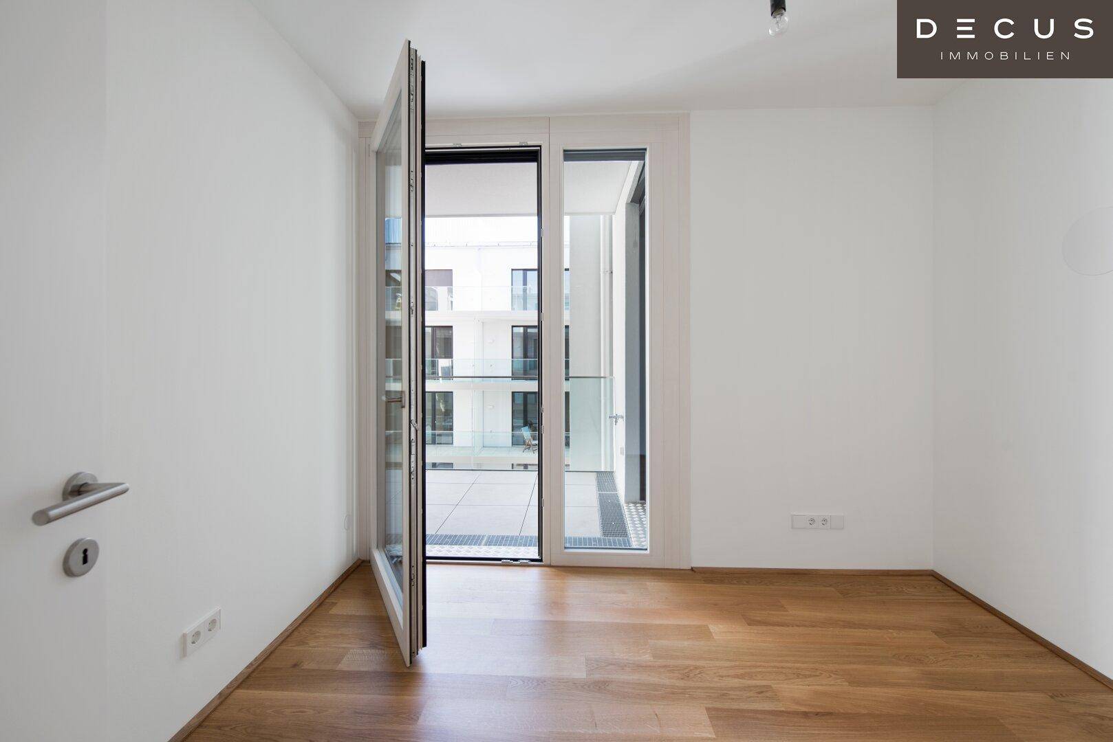 Lichtdurchfluteter Raum mit Holzboden und Zugang zu einem Balkon mit Blick auf den Innenhof.