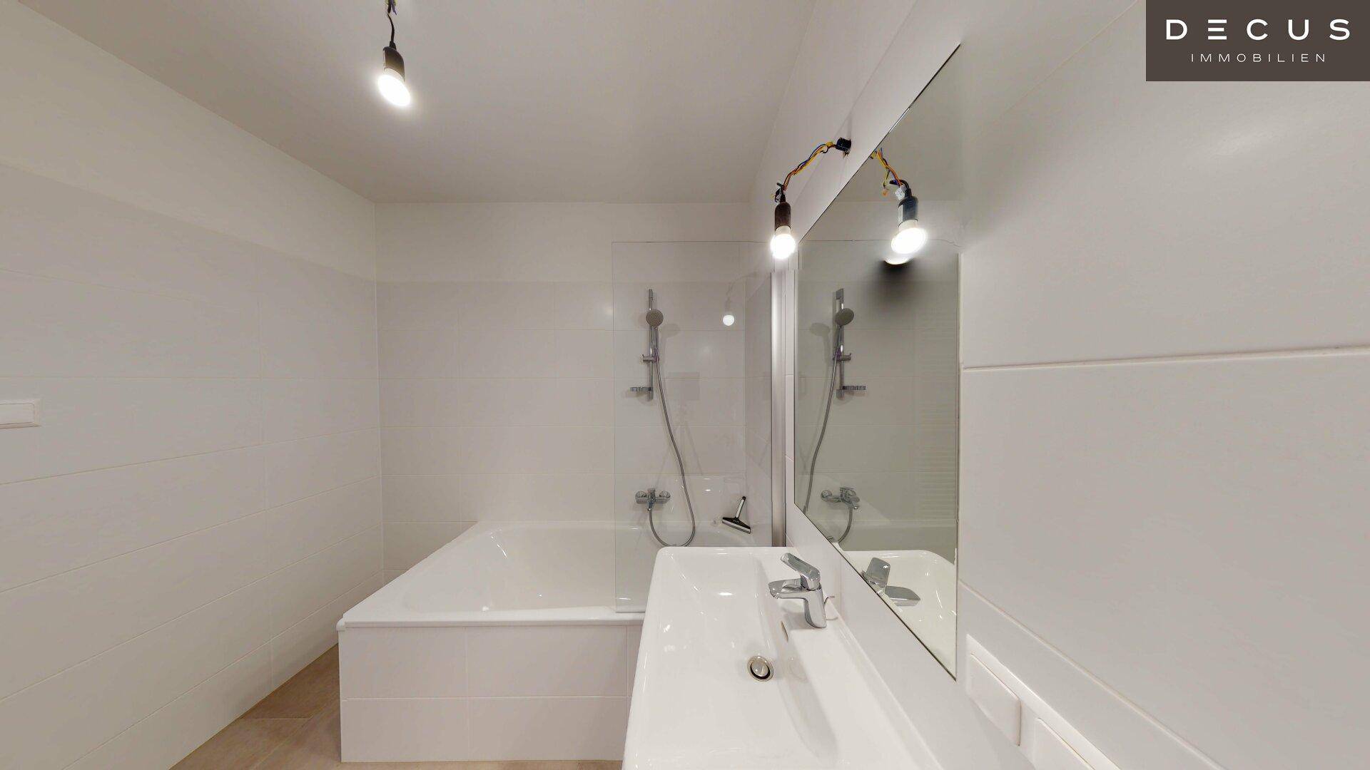 Modernes Badezimmer mit Badewanne, Einzelwaschbecken und großem Spiegel in hellen Fliesen.