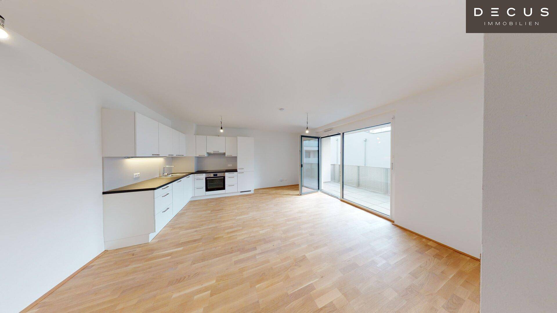 Heller offener Wohnbereich mit integrierter Küche, Parkettboden und Zugang zum Balkon.