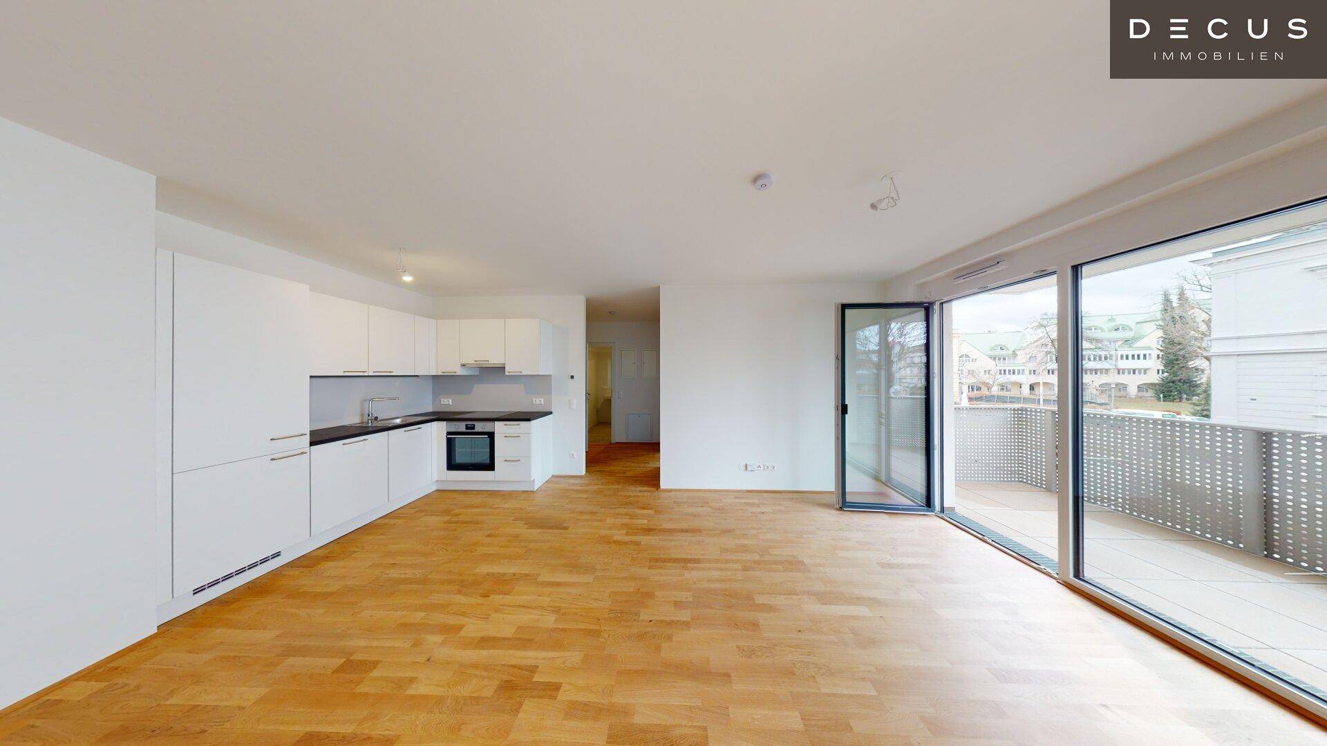 Moderner Wohnbereich mit Einbauküche, Parkettboden und viel Tageslicht durch große Fenster.