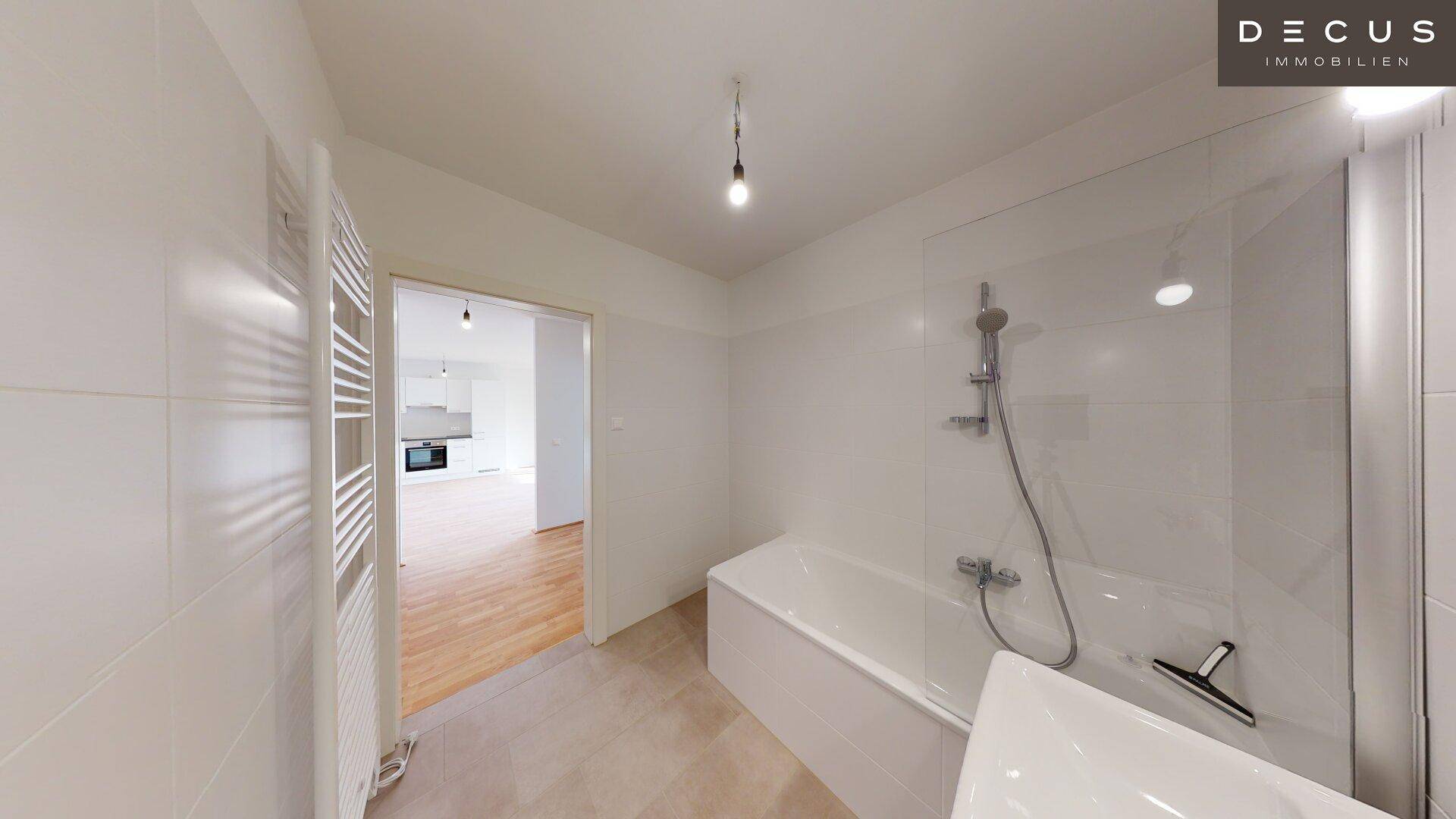 Helles Badezimmer mit Badewanne und Duschvorrichtung, Blick in den angrenzenden Wohnbereich.