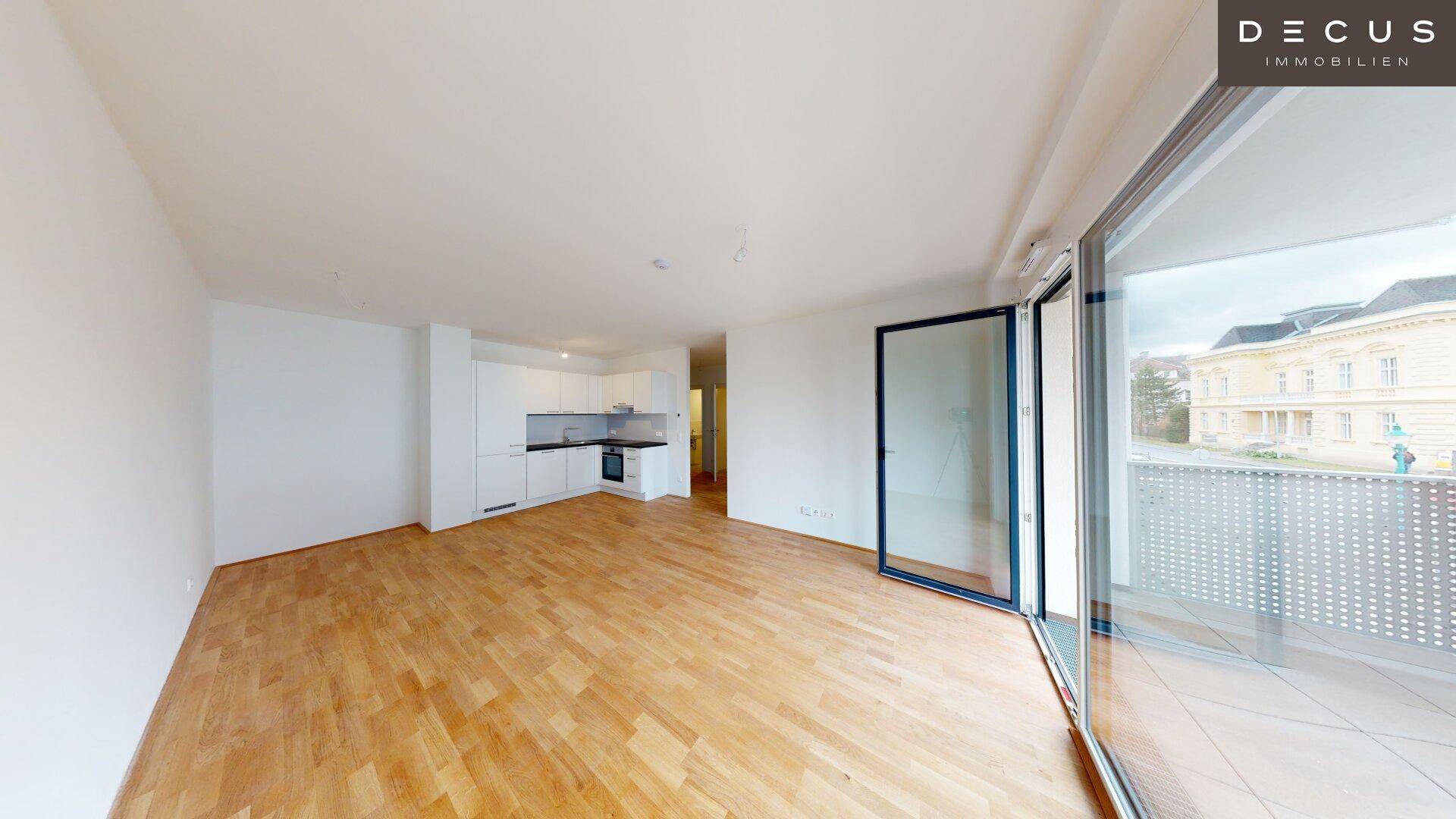 Offener Wohnbereich mit integrierter Küchenzeile, Parkettboden und Zugang zu einem Balkon.