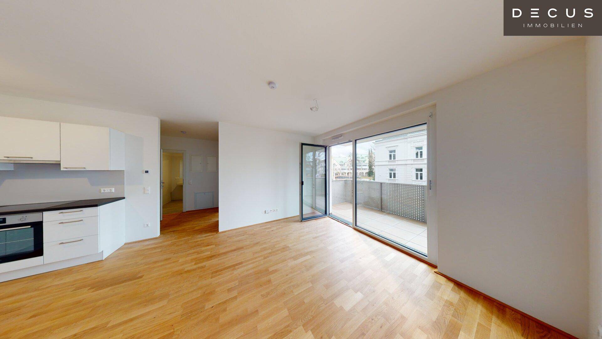 Heller Wohn- und Essbereich mit moderner Küchenzeile und großen Fenstern zum Balkon.